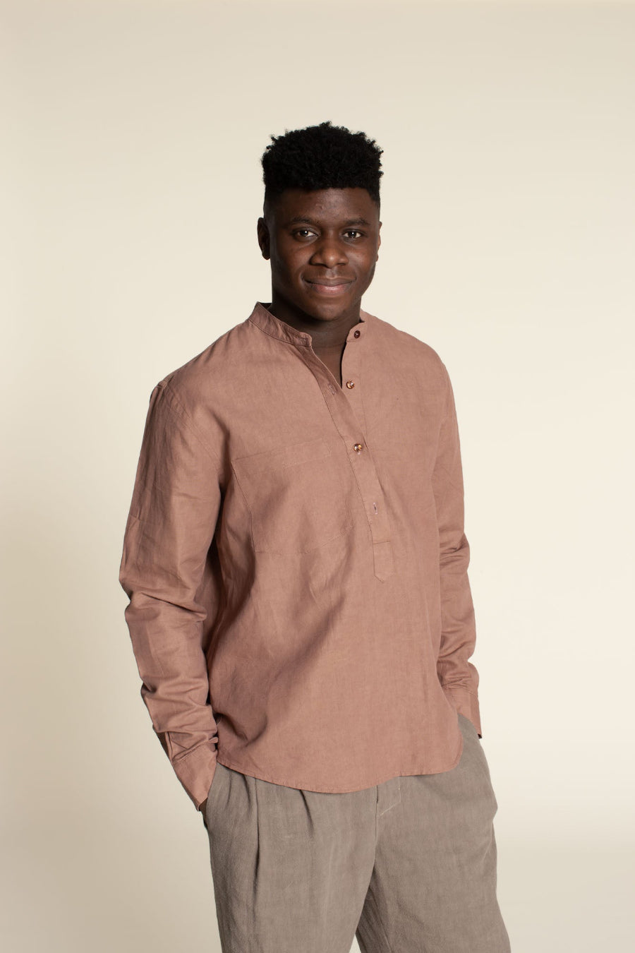 Man wearing a brown long-sleeve shirt and beige pants against a beige background